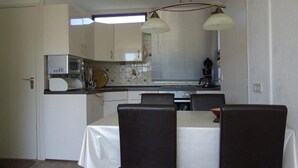A compact kitchen with white cabinets, a microwave, and a dining area with a table and chairs. - Family Bungalow Near the Beach and sea (Sint Maartensvlotbrug)