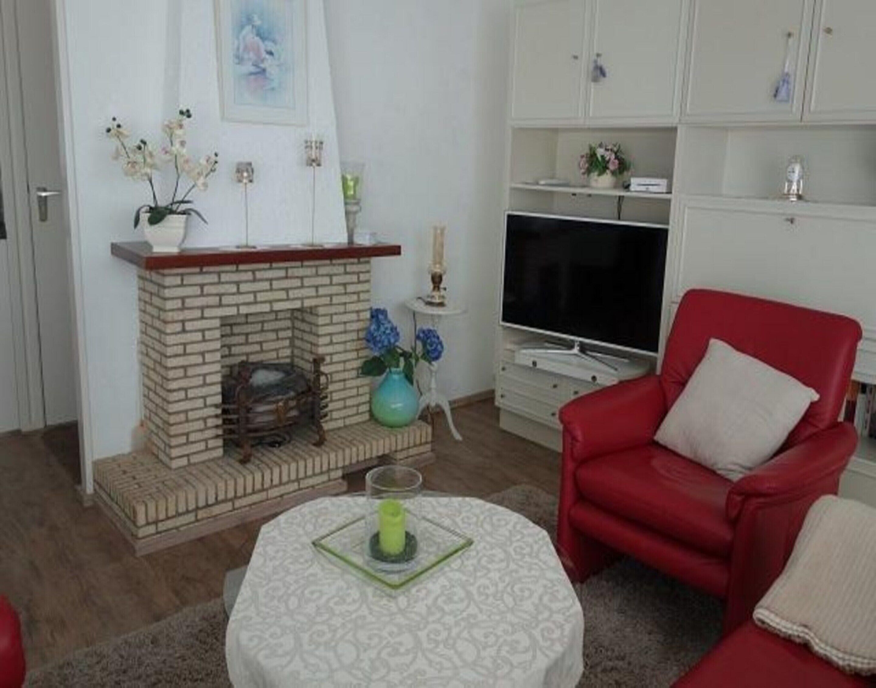 A living room with a brick fireplace, a red armchair, a television, and a white cabinet with shelves.