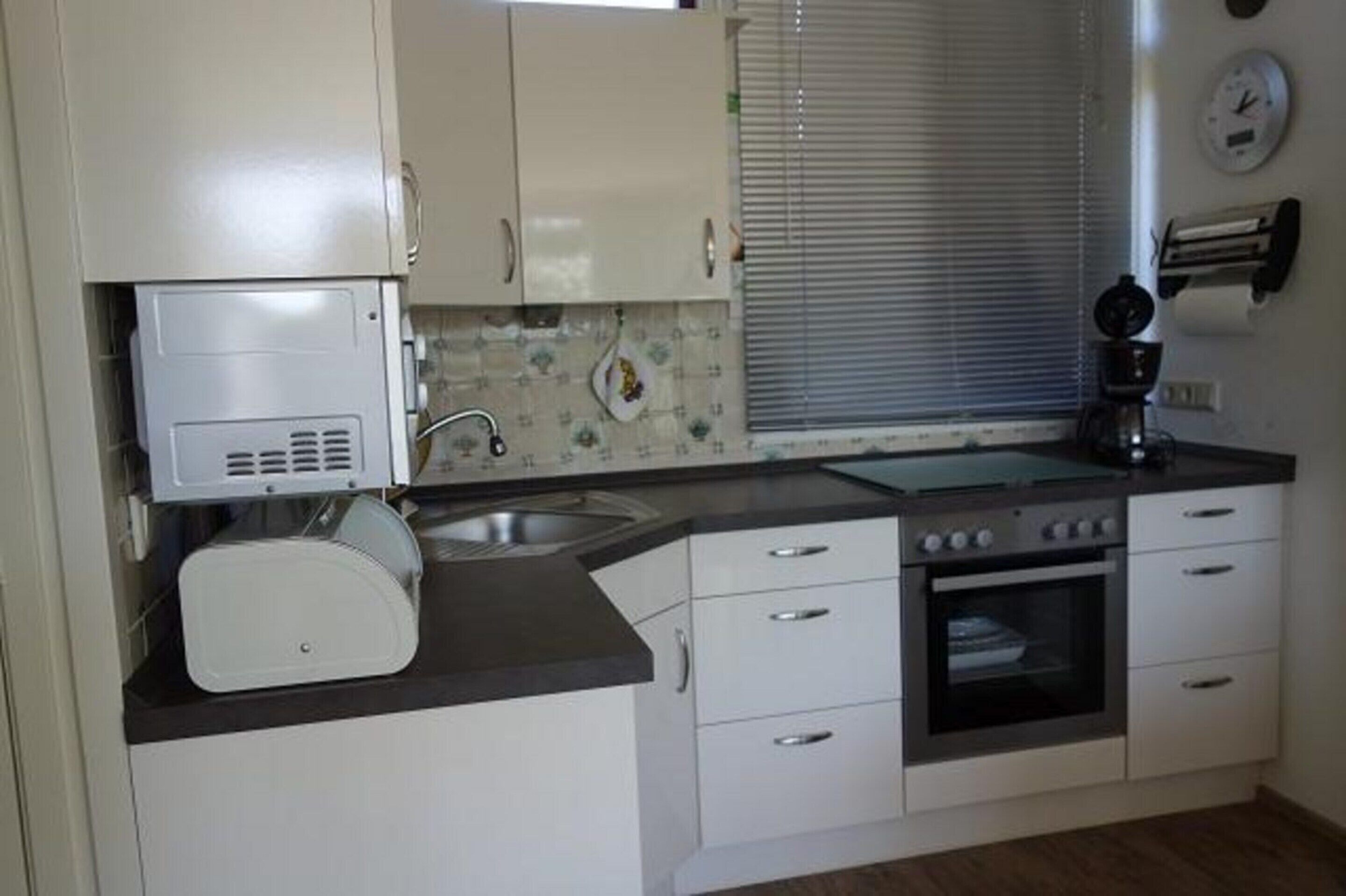 A compact kitchen with white cabinets, a built-in oven, and a coffee maker.