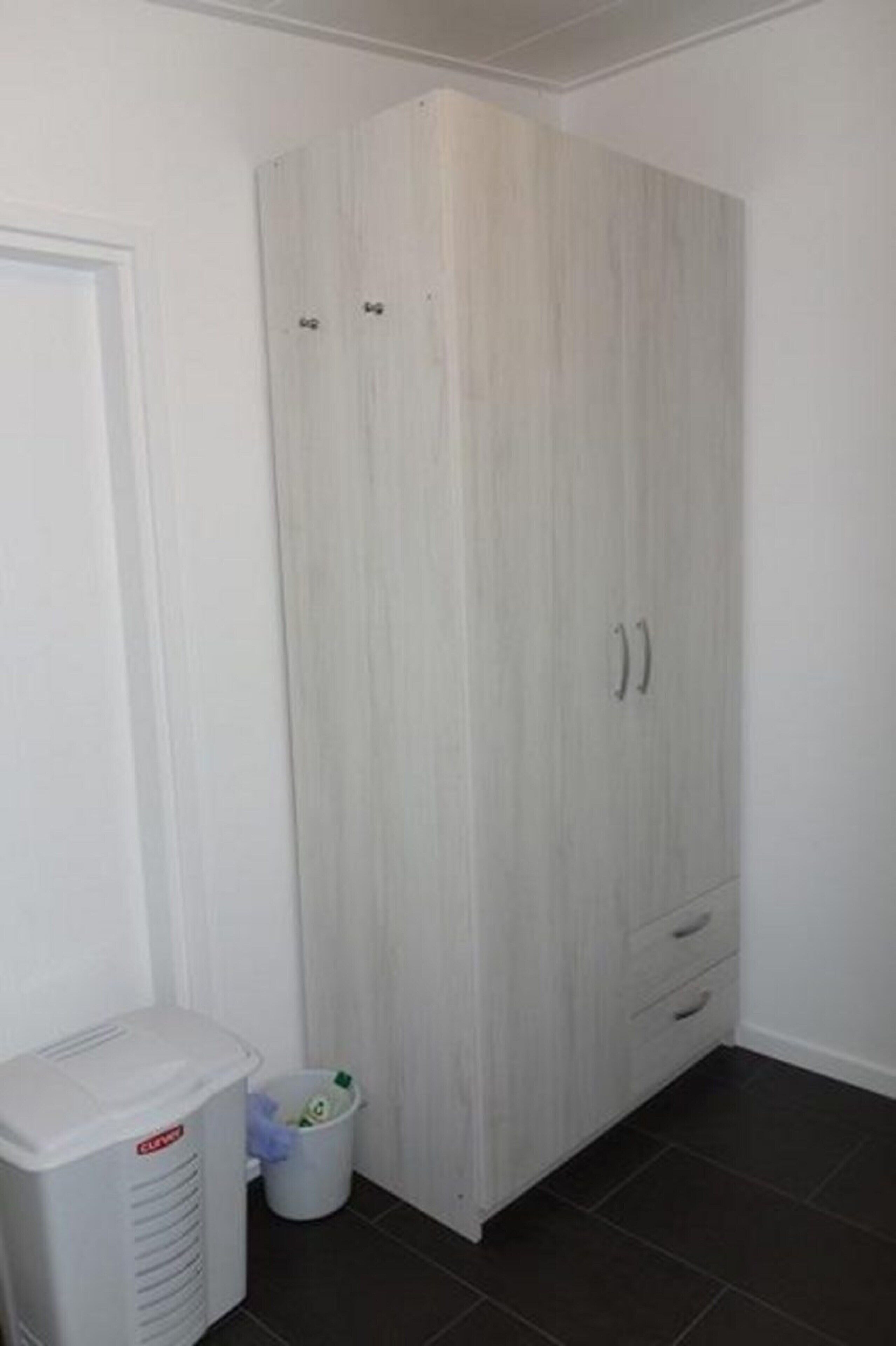 A room with a white wardrobe, a white laundry basket, and a white appliance.