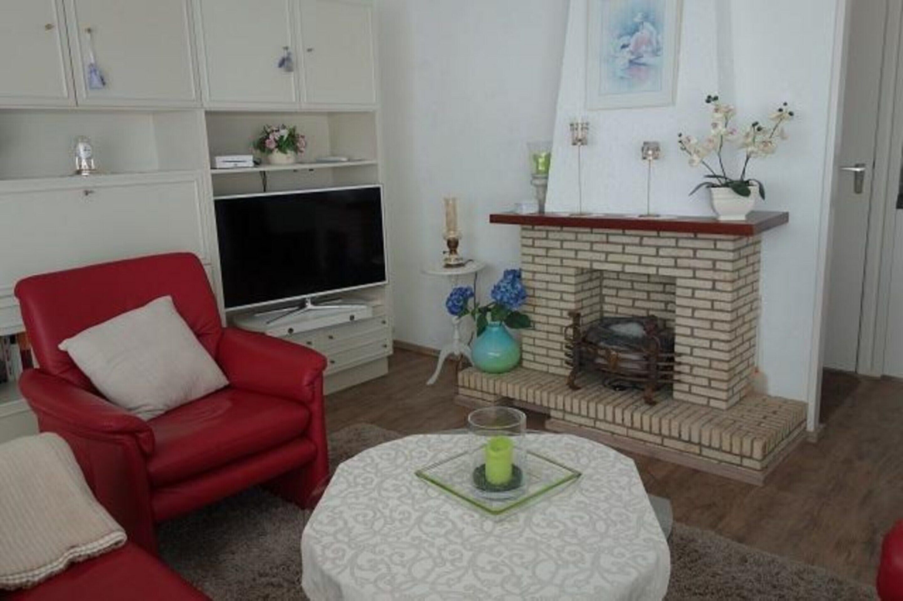 A living room with a red armchair, a television, a fireplace, and a small table with a candle.