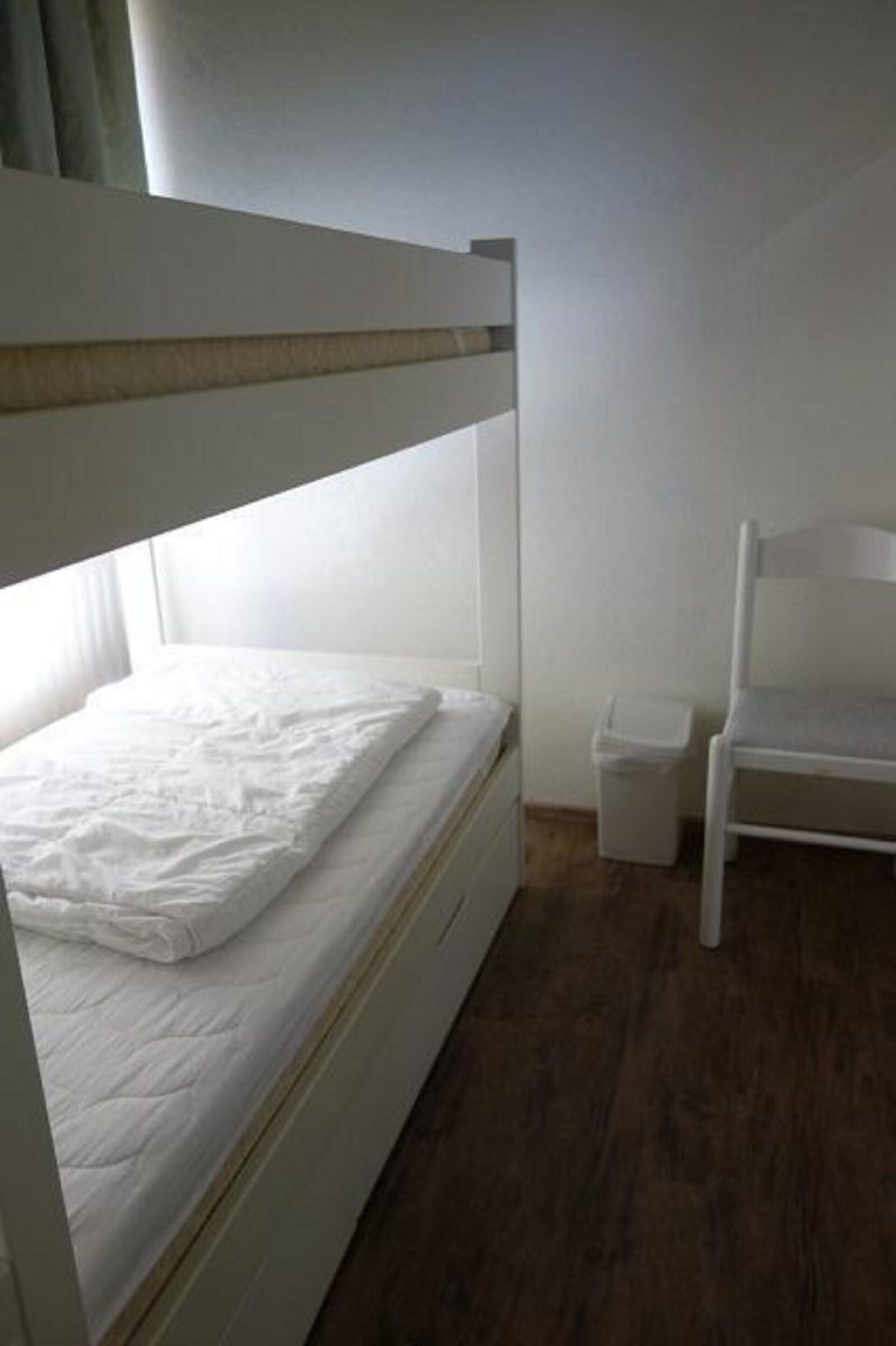 Un lit superposé avec un matelas blanc et une petite chaise blanche à côté.