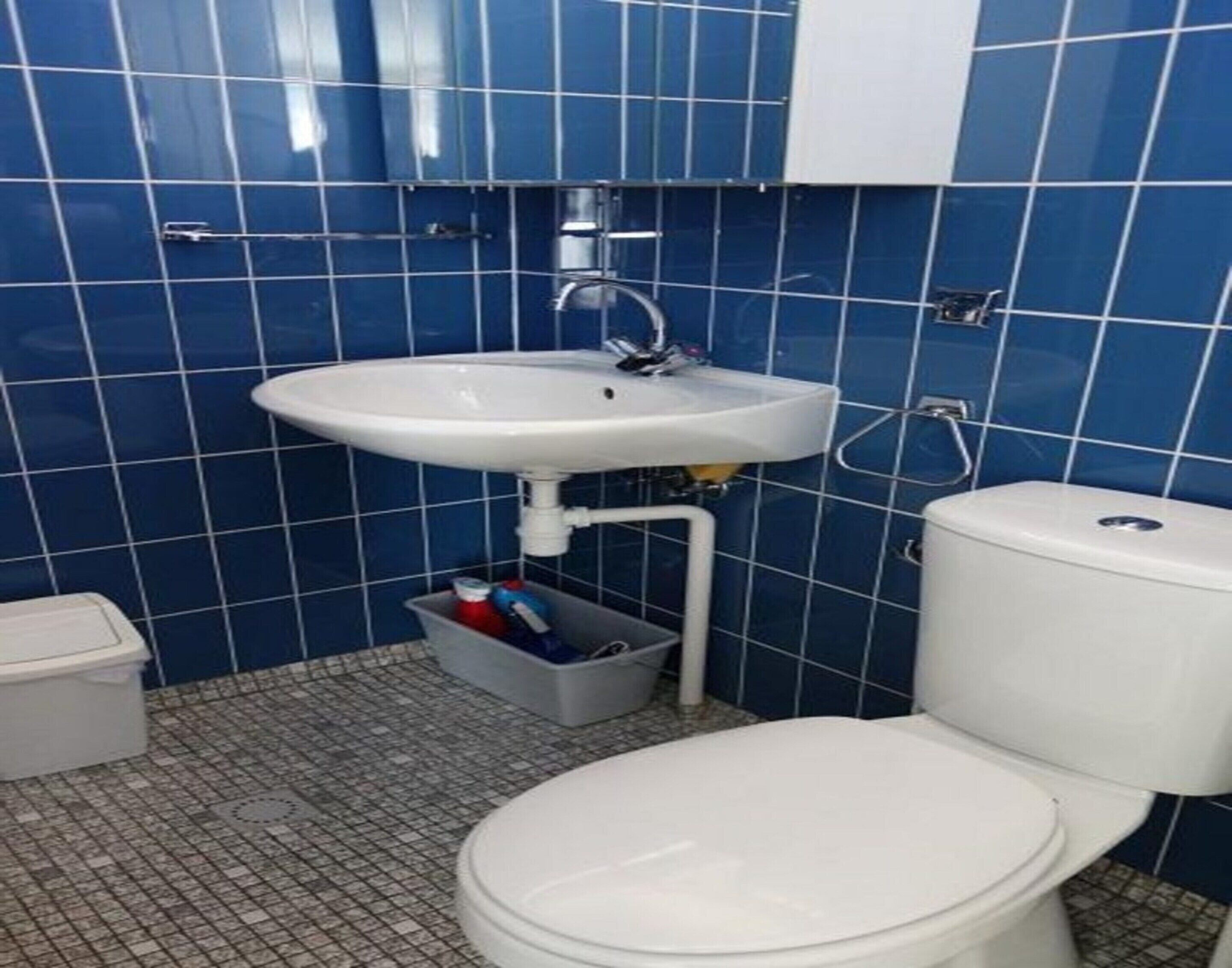 A bathroom with a white sink, blue tiled walls, and a white toilet.
