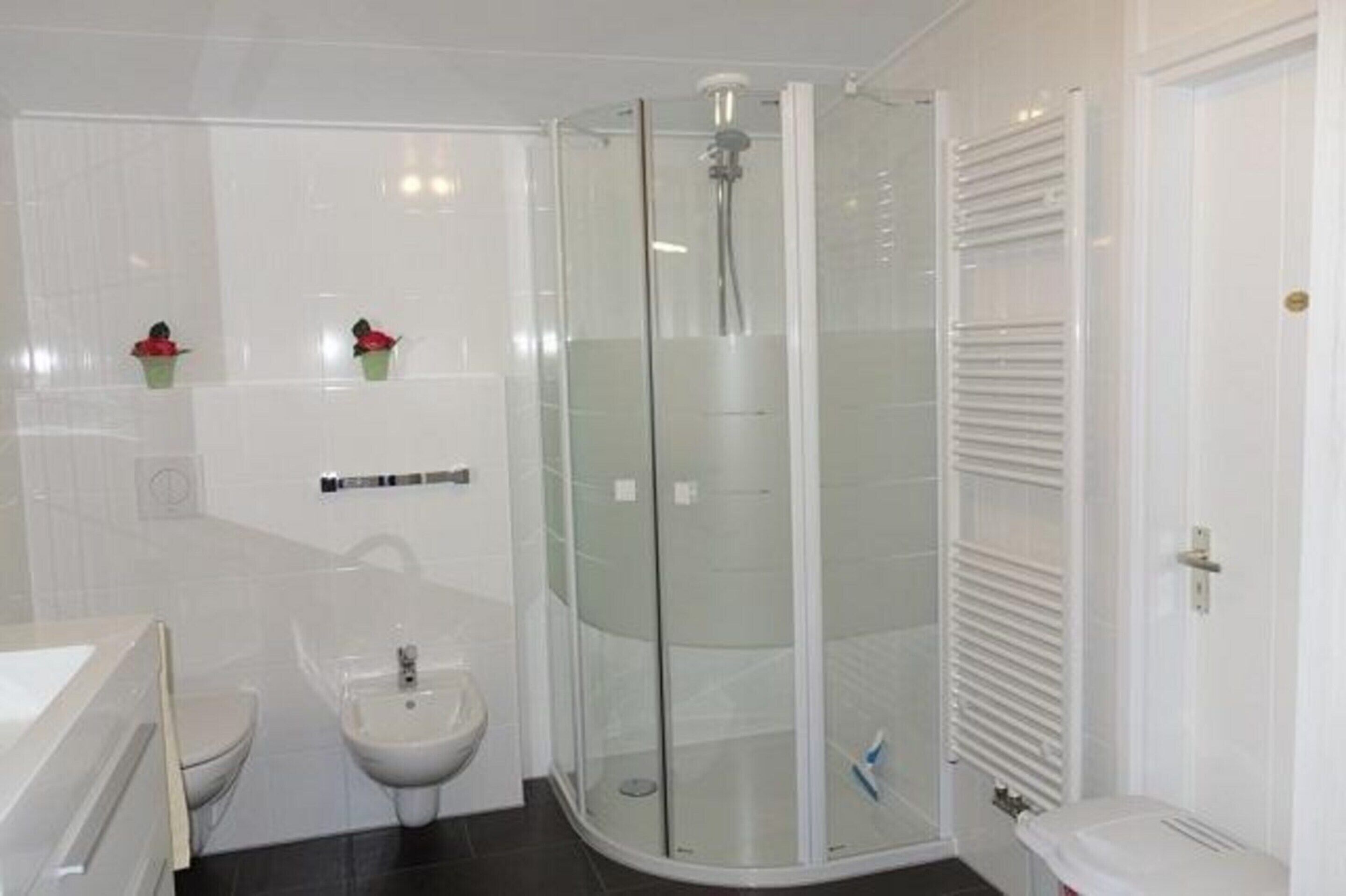 Ein modernes Badezimmer mit einer gläsernen Duschkabine, einem Bidet, einer Toilette und einem Waschbecken mit Spiegel.