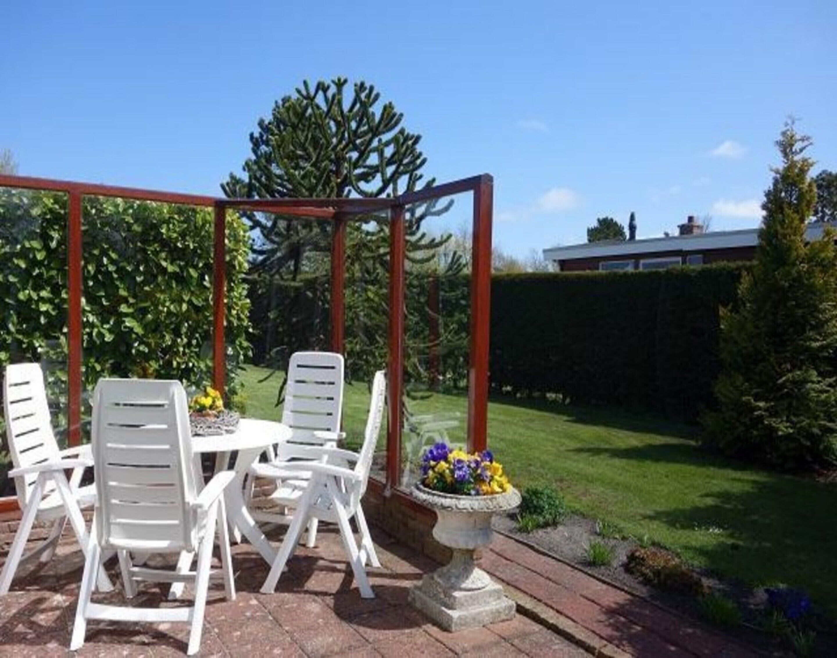 Eine Terrasse mit weißen Plastikstühlen und einem Tisch, umgeben von einer Holz-Pergola.