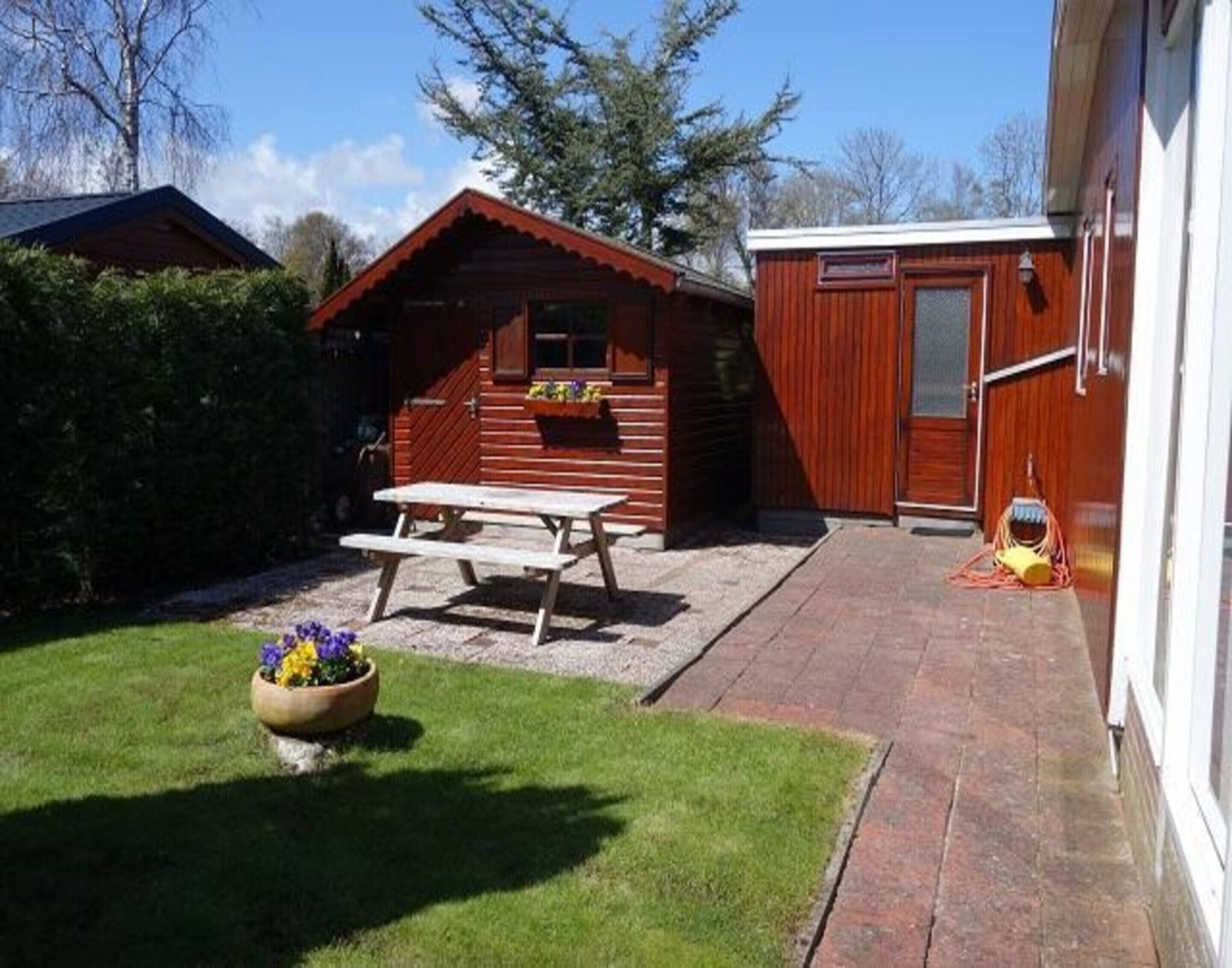A wooden cabin with a picnic table and a flower pot in the yard.