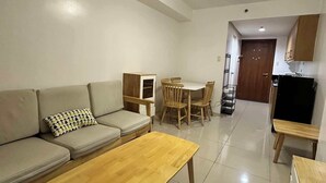 A living room with a sofa, a wooden coffee table, a dining table with chairs, and a TV stand. - Shell Residences by Staycation (Pasay)
