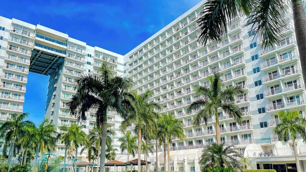 A multi-story hotel with a pool area, palm trees, and a clear blue sky. - Shell Residences by Staycation (Pasay)