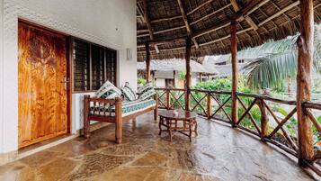 Traditional-style room with a thatched roof and wooden beams, featuring a stone floor and a cozy bench with patterned cushions.
