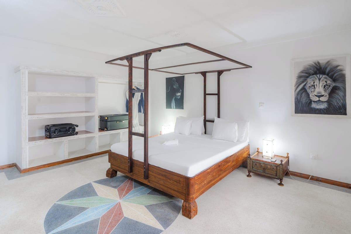 Un dormitorio con cama con dosel, una mesita de noche con lámpara, un armario y una alfombra colorida.