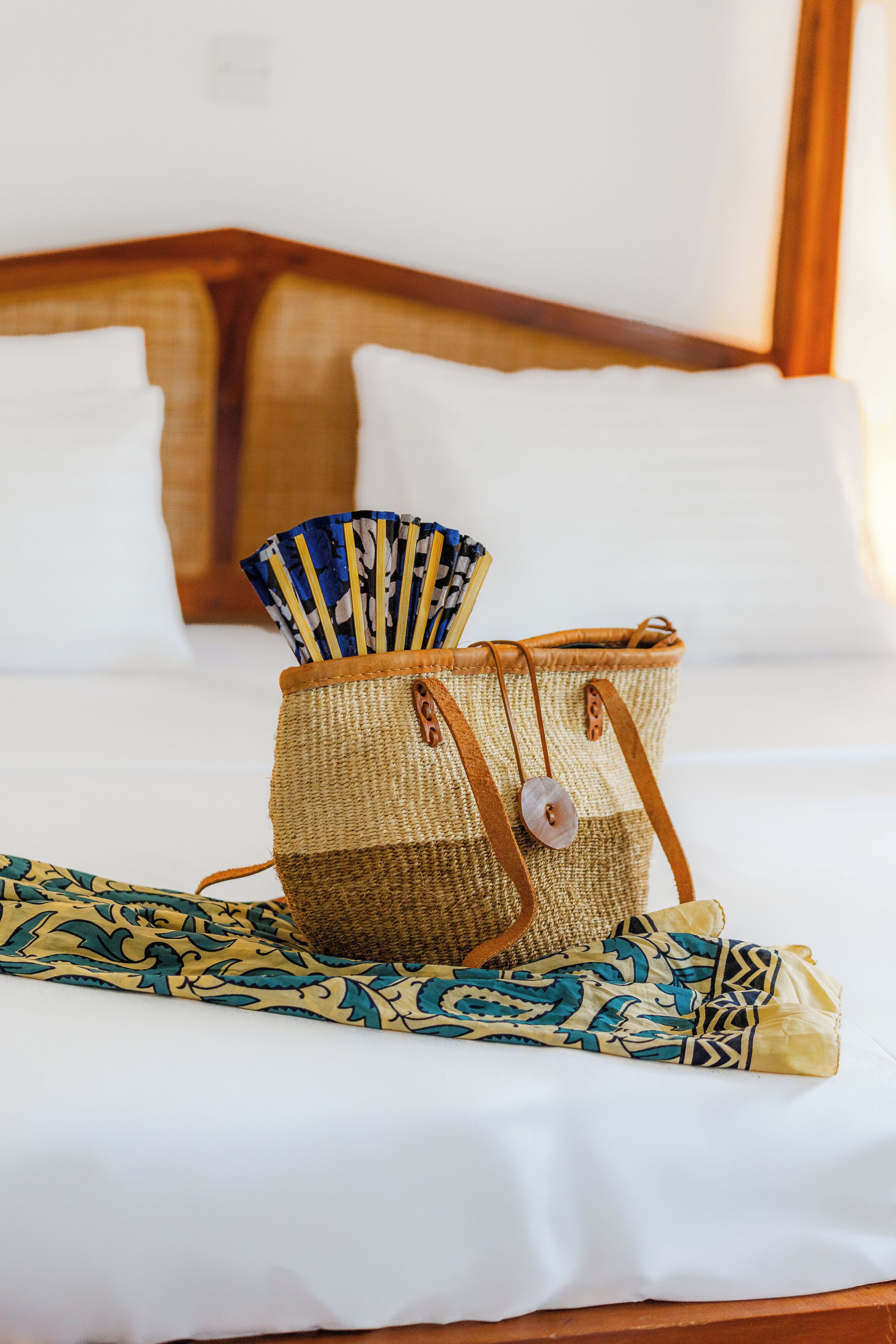 Un lit avec du linge de lit blanc, un panier tressé avec une anse marron et un tissu à motifs sur le lit.