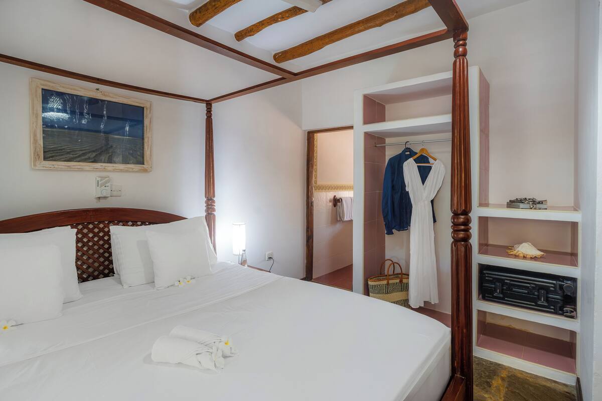 Habitación de hotel con una cama grande, cabecero de madera, un cuadro en la pared y un armario con ropa colgada.