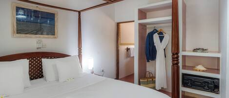 Une chambre d’hôtel avec un grand lit, une tête de lit en bois, un tableau au mur et une armoire contenant des vêtements suspendus.