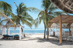 A beach scene with palm trees, a wooden structure with chairs, and a view of the ocean. - Exploreans Beach Club & Villas Watamu (Malindi)