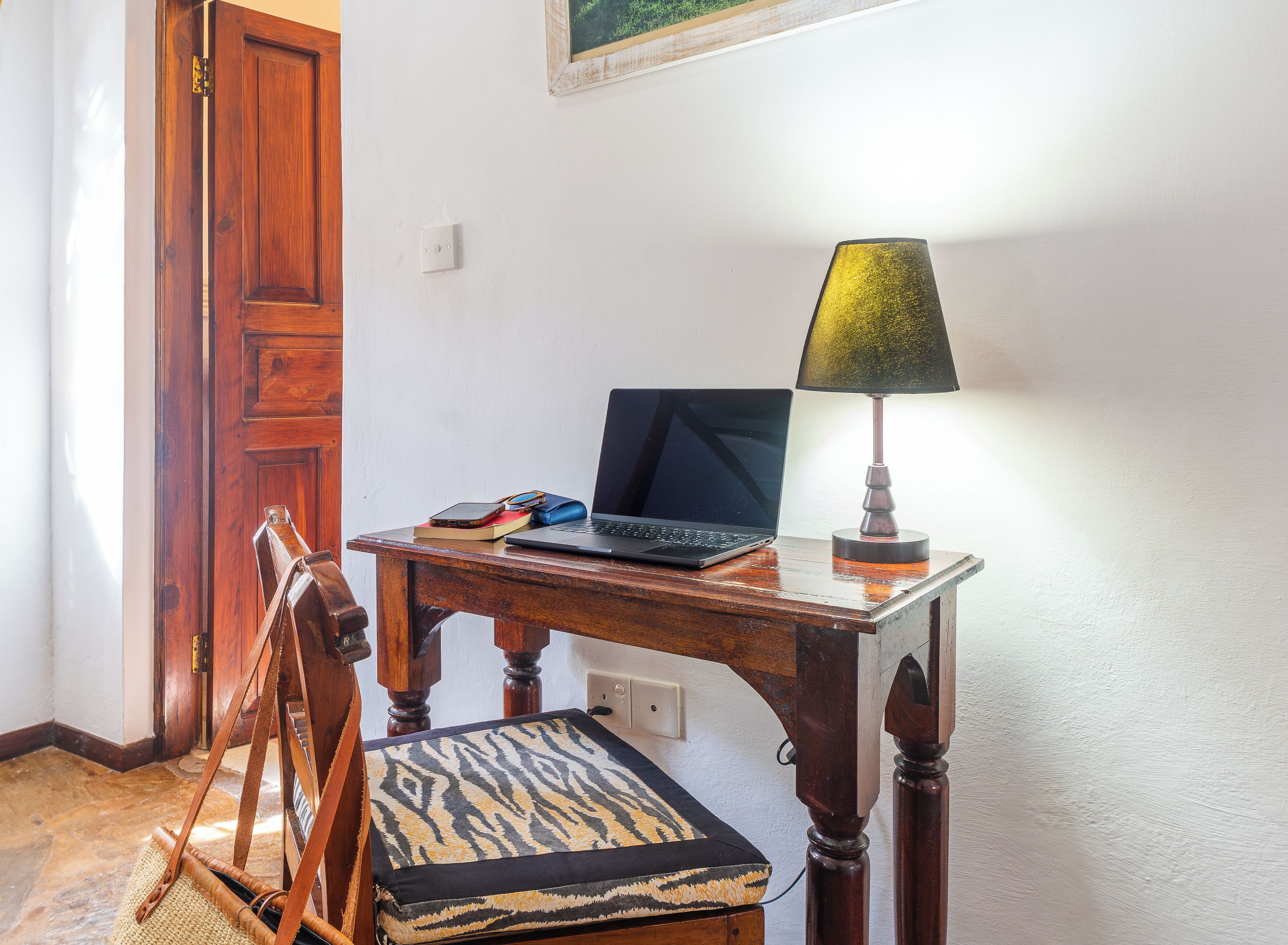 A wooden desk with a laptop, a lamp, and a chair with a patterned cushion.