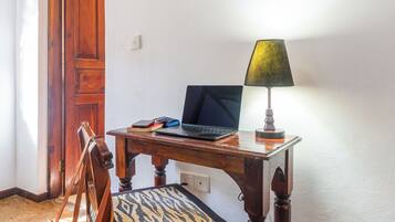A wooden desk with a laptop, a lamp, and a chair with a patterned cushion.