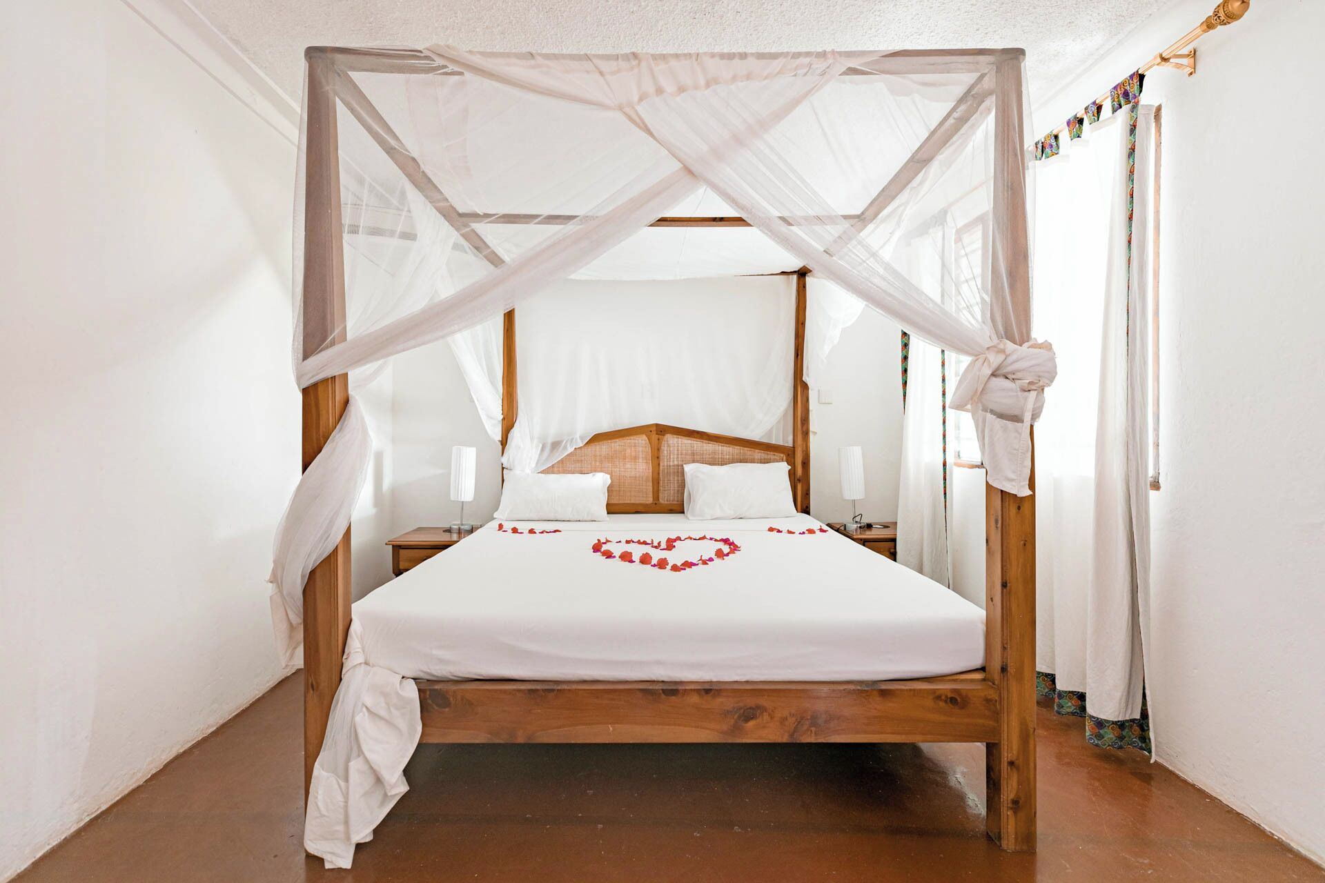 A wooden four-poster bed with a white canopy, a heart-shaped decoration on the bed, and a wooden headboard.