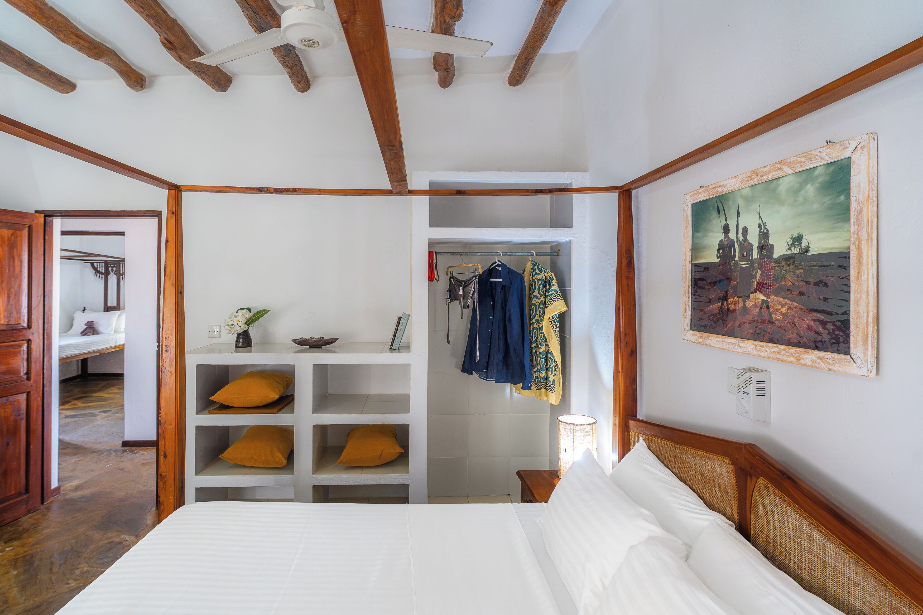 Une chambre à coucher avec un lit, des murs blancs, des poutres en bois, une armoire et un tableau.