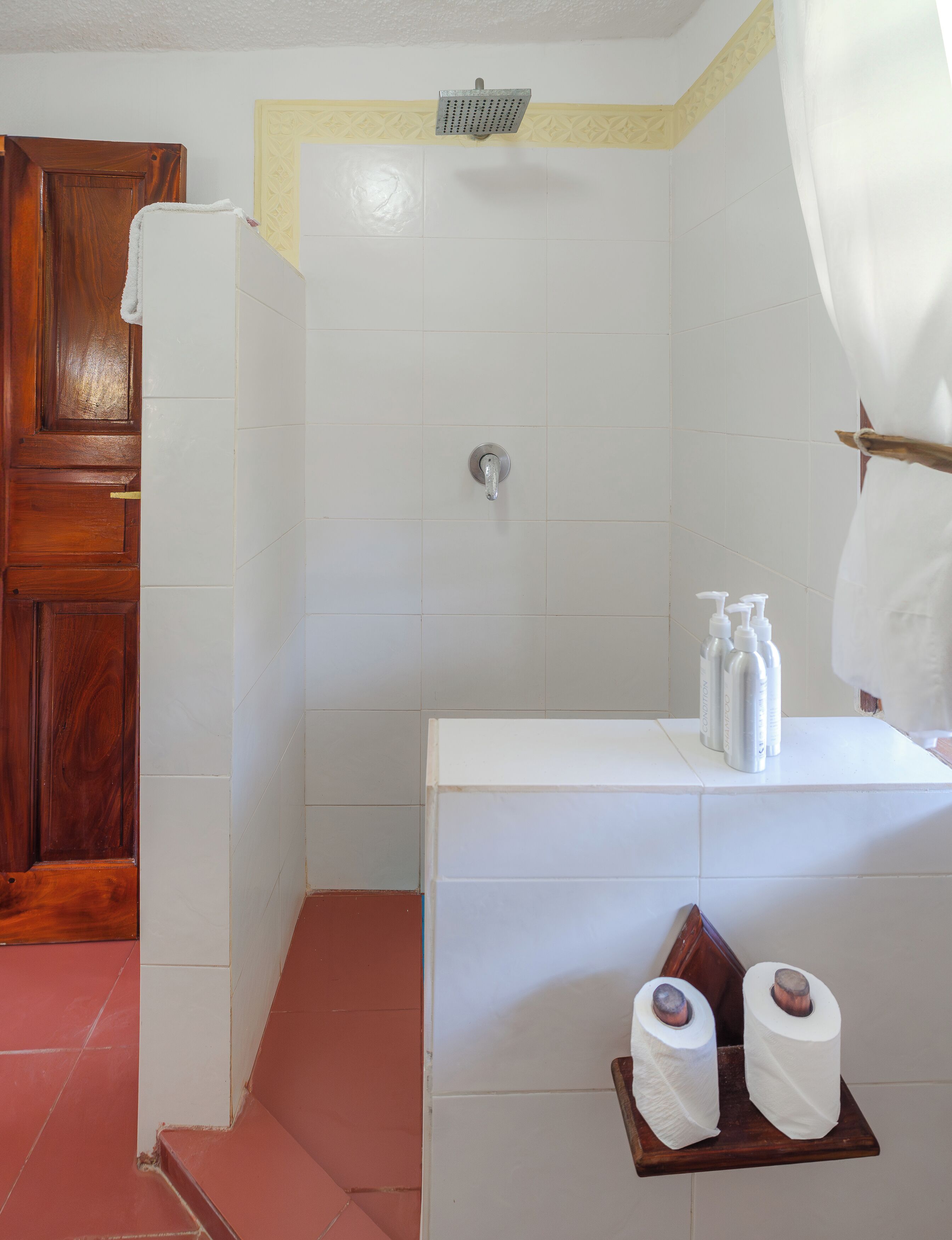 A bathroom with a shower, toilet paper, and toiletries on a shelf.