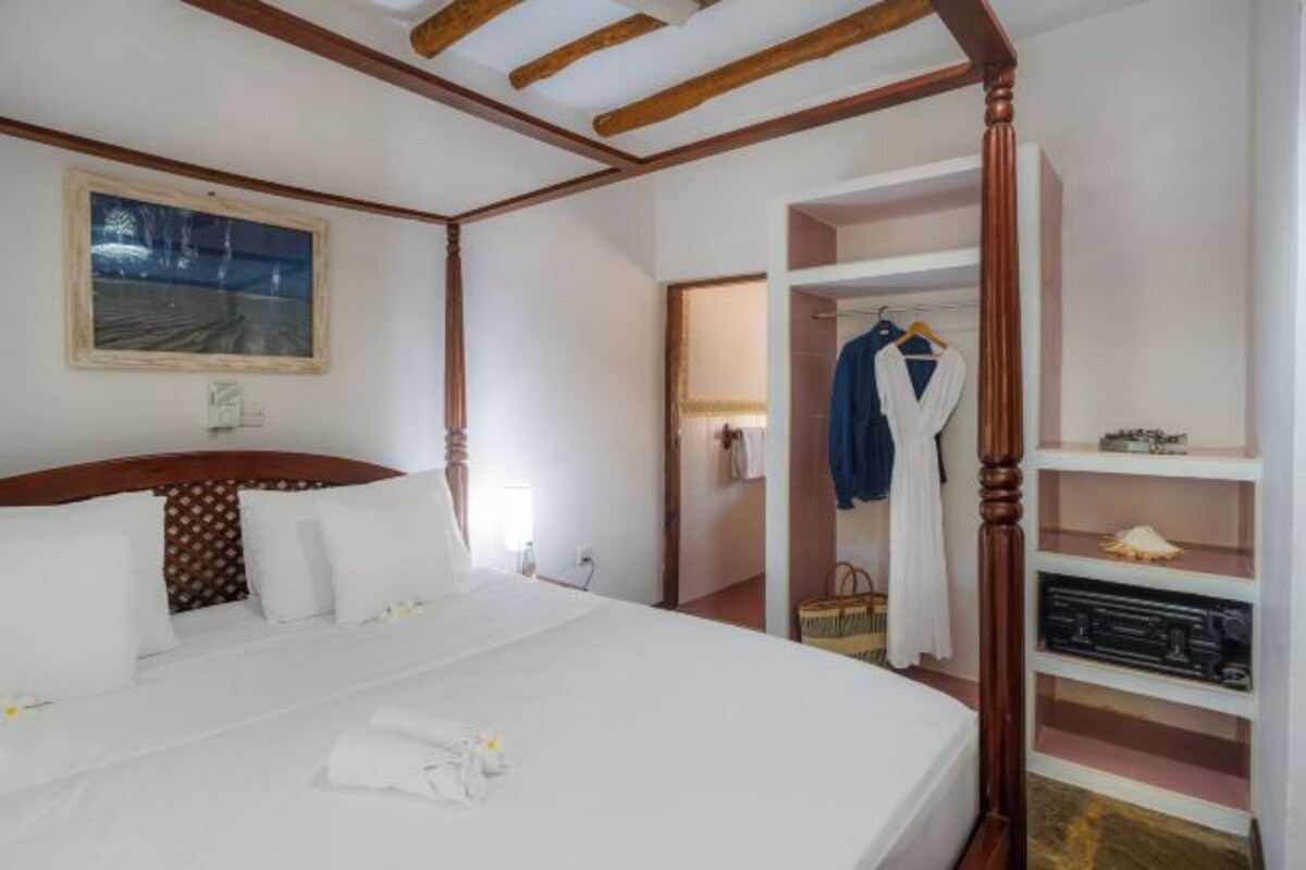 A hotel room with a large bed, a wardrobe, a mirror, and a painting on the wall.