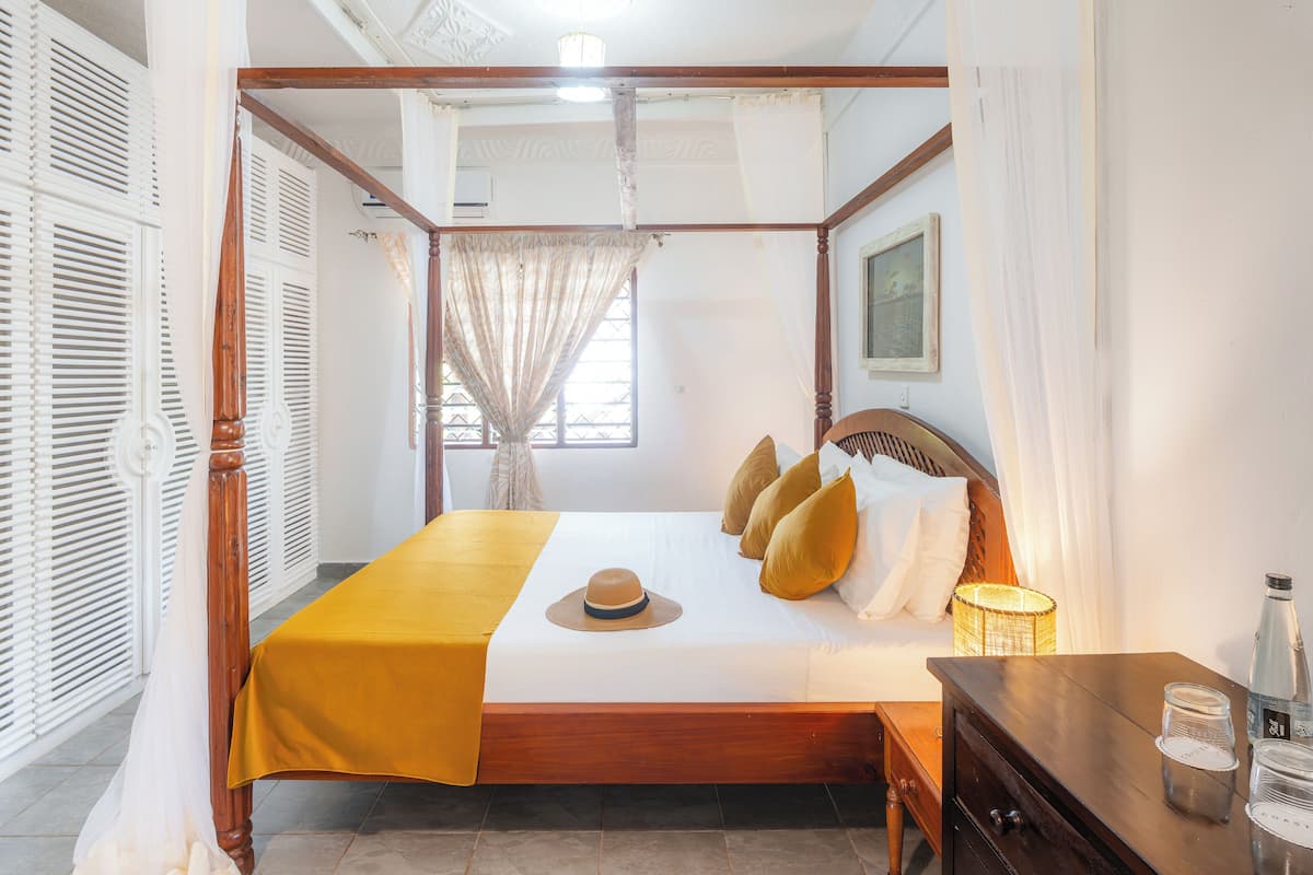 Una cama con dosel, con un edredón amarillo, una mesita de noche de madera y una mesita con una lámpara y una botella.