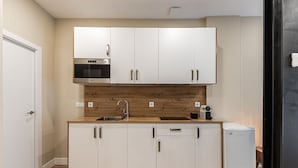 Cocina compacta con armarios blancos, microondas integrado, pileta y heladera pequeña.