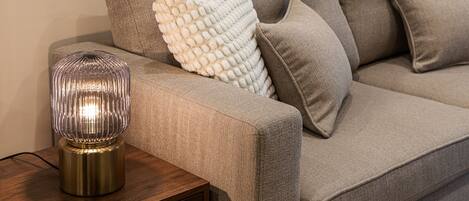 A modern living room with a sofa, a white textured pillow, and a metallic lamp on a wooden side table.
