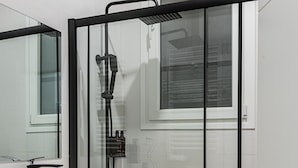 Un baño moderno con cabina de ducha de vidrio, un lavamanos blanco y un mueble de tocador de madera.