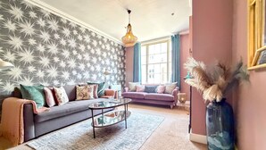 A living room with a grey sofa, a round coffee table, and a patterned wallpaper. - Bridge Street Rows Apartment -  a house that sleeps 8 guests  in 3 bedrooms (Chester)