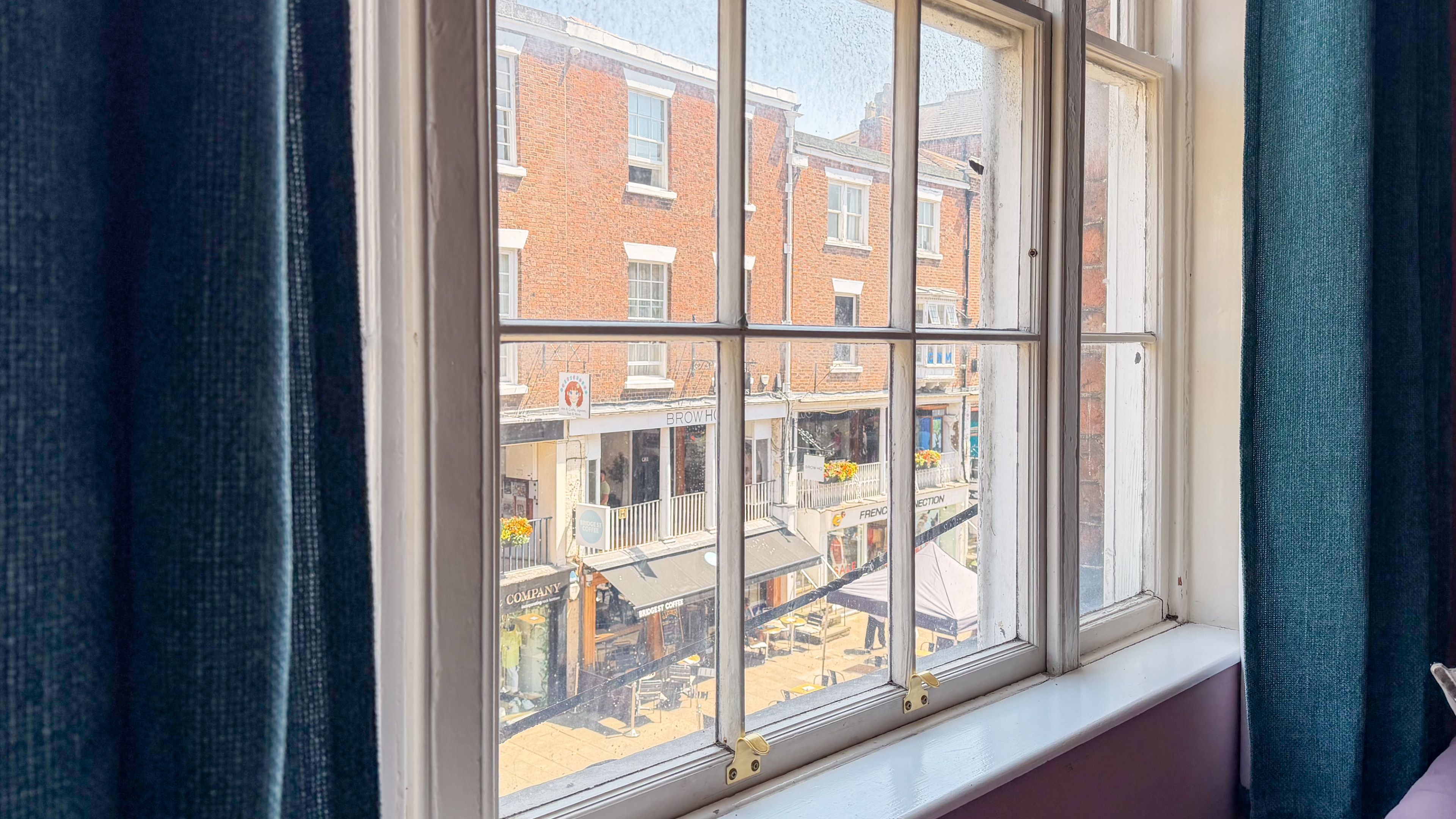 Una ventana con vista a un edificio de ladrillo y un balcón lleno de flores.