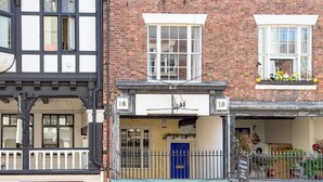 A building with a brick facade, numbered 18, featuring a blue door and a small porch area. - Bridge Street Rows Apartment -  a house that sleeps 8 guests  in 3 bedrooms (Chester)