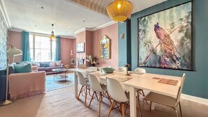A modern living room with a dining area, a large peacock painting, and a chandelier. - Bridge Street Rows Apartment -  a house that sleeps 8 guests  in 3 bedrooms (Chester)