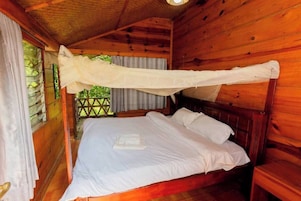 Quarto de cabana de madeira com cama, roupa de cama branca e mosquiteiro.