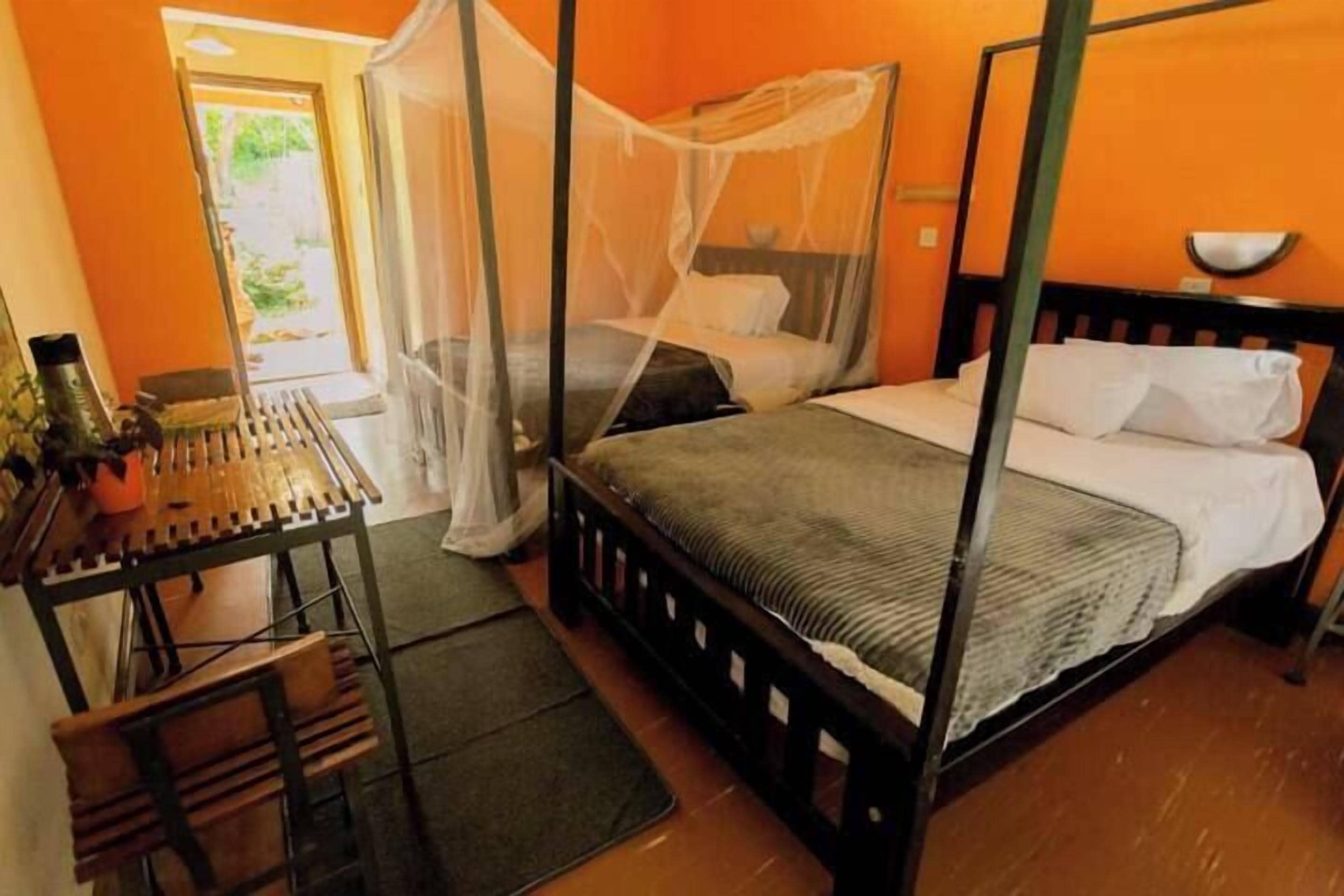 A room with a four-poster bed, a small table with chairs, and a view of the outdoors.