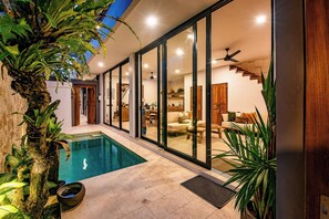 A modern house with a swimming pool, sliding glass doors leading to a living area, and a staircase. - Sister Suites (Seminyak)