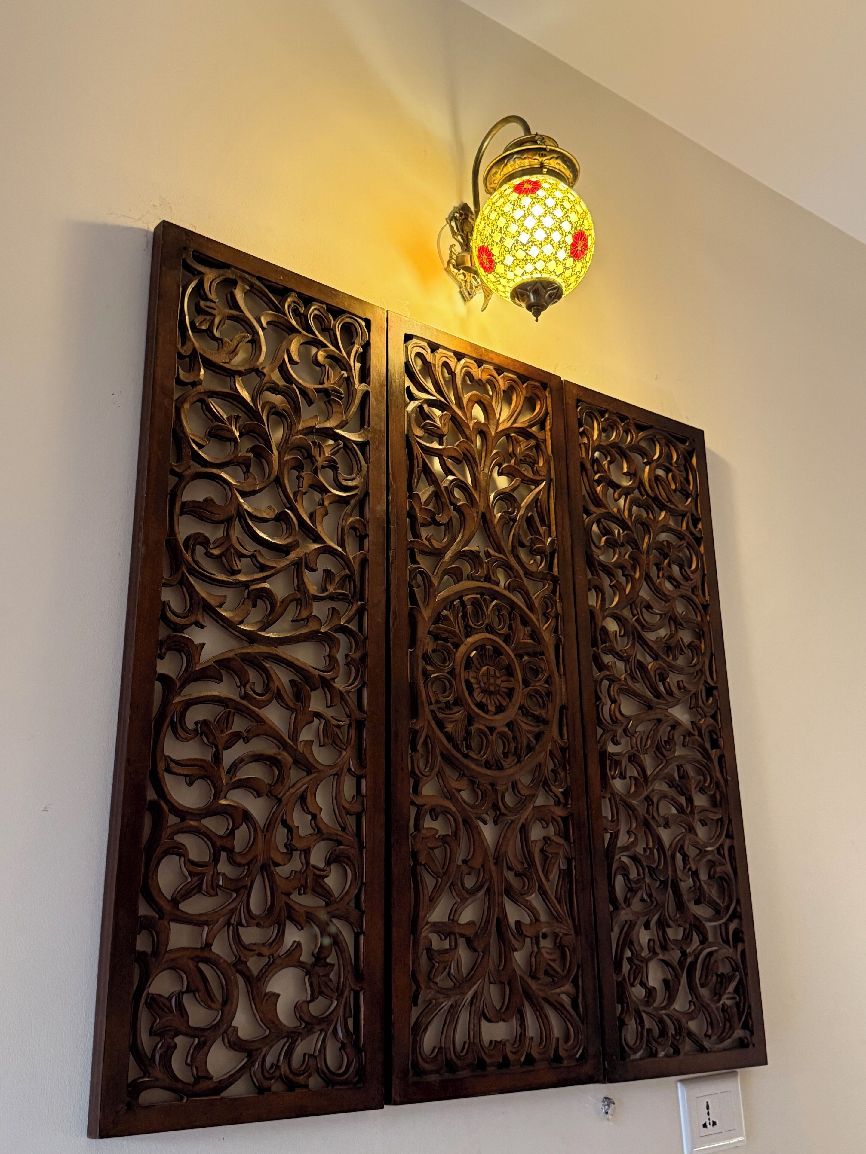 Un panel decorativo fijado a la pared con tallas intrincadas y una lámpara de pared encima.