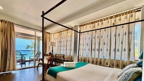 A hotel room with a large bed, a balcony with a view, and a seating area with a table and chairs.