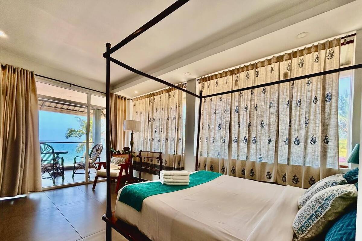 A hotel room with a large bed, a balcony with a view, and a seating area with a table and chairs.