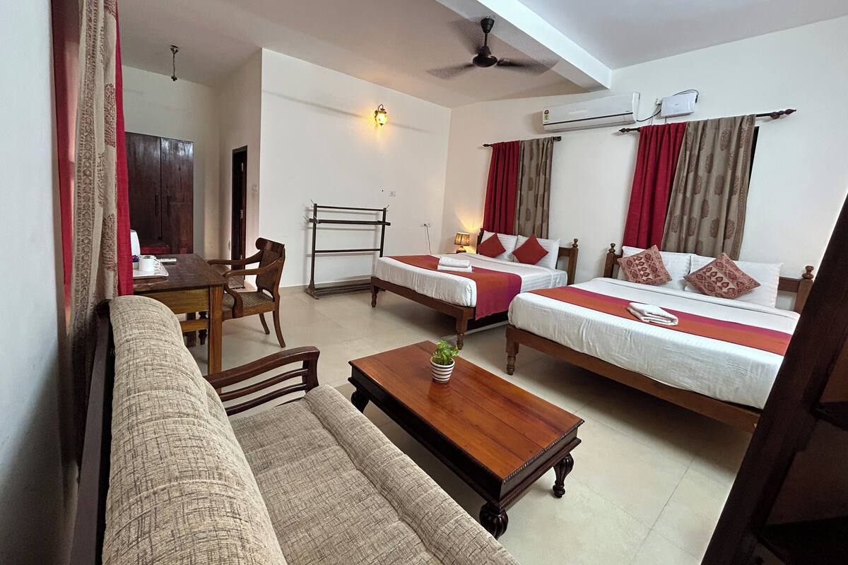 A hotel room with two single beds, a sofa, a wooden coffee table, and a desk with a chair.