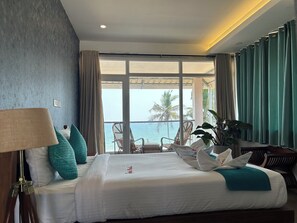 A hotel room with a large bed, a view of the sea, and a balcony with chairs.