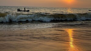 Una playa al atardecer con olas y un barco a lo lejos.