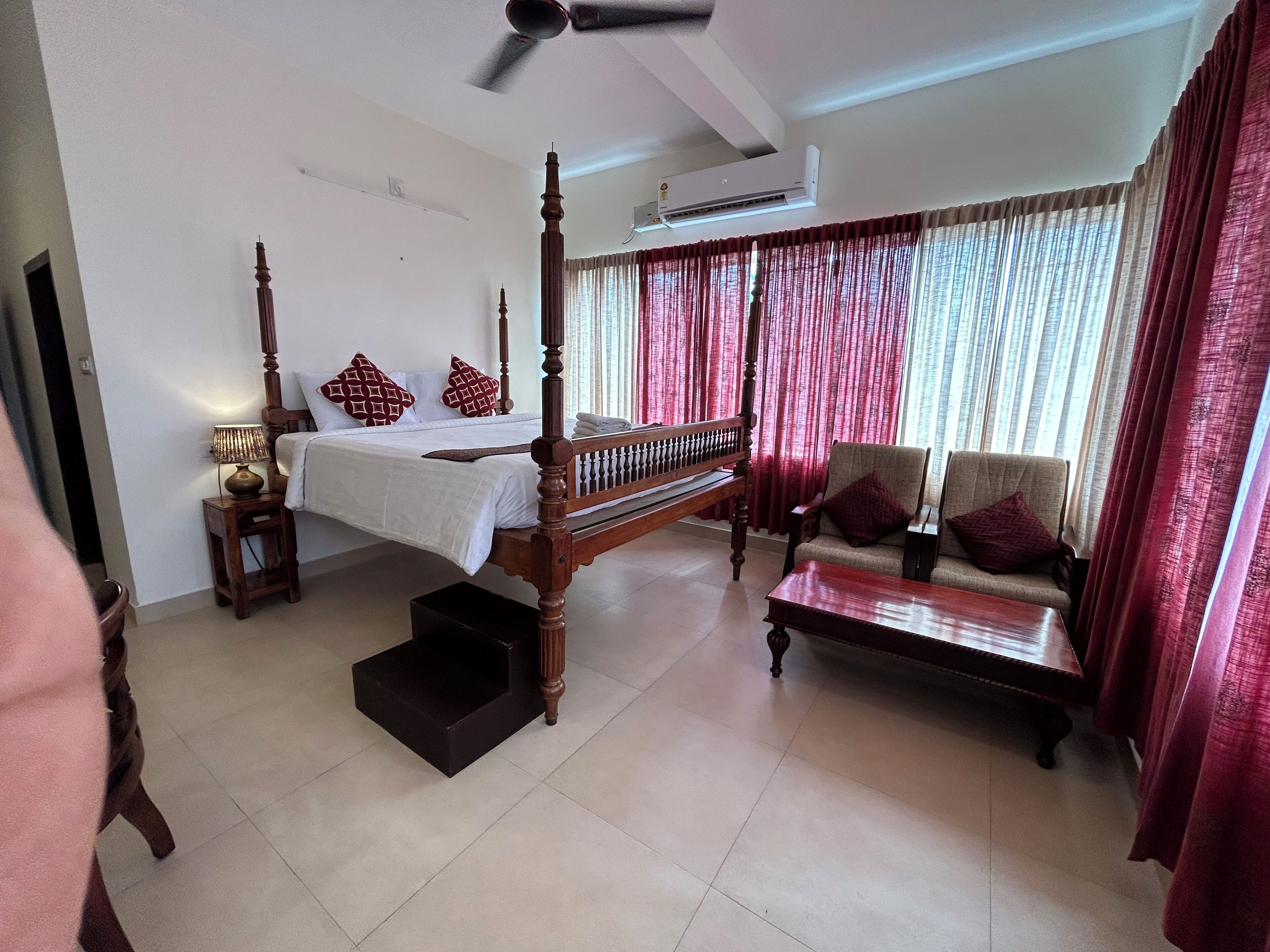 A bedroom with a four-poster bed, a sofa, a small table, and a ceiling fan.