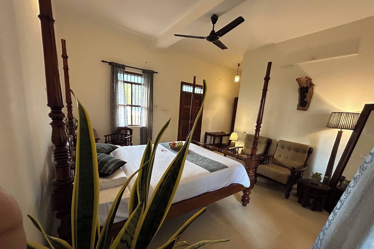 A spacious bedroom with a large bed, a sitting area with a sofa and armchairs, a ceiling fan, and a window with curtains.