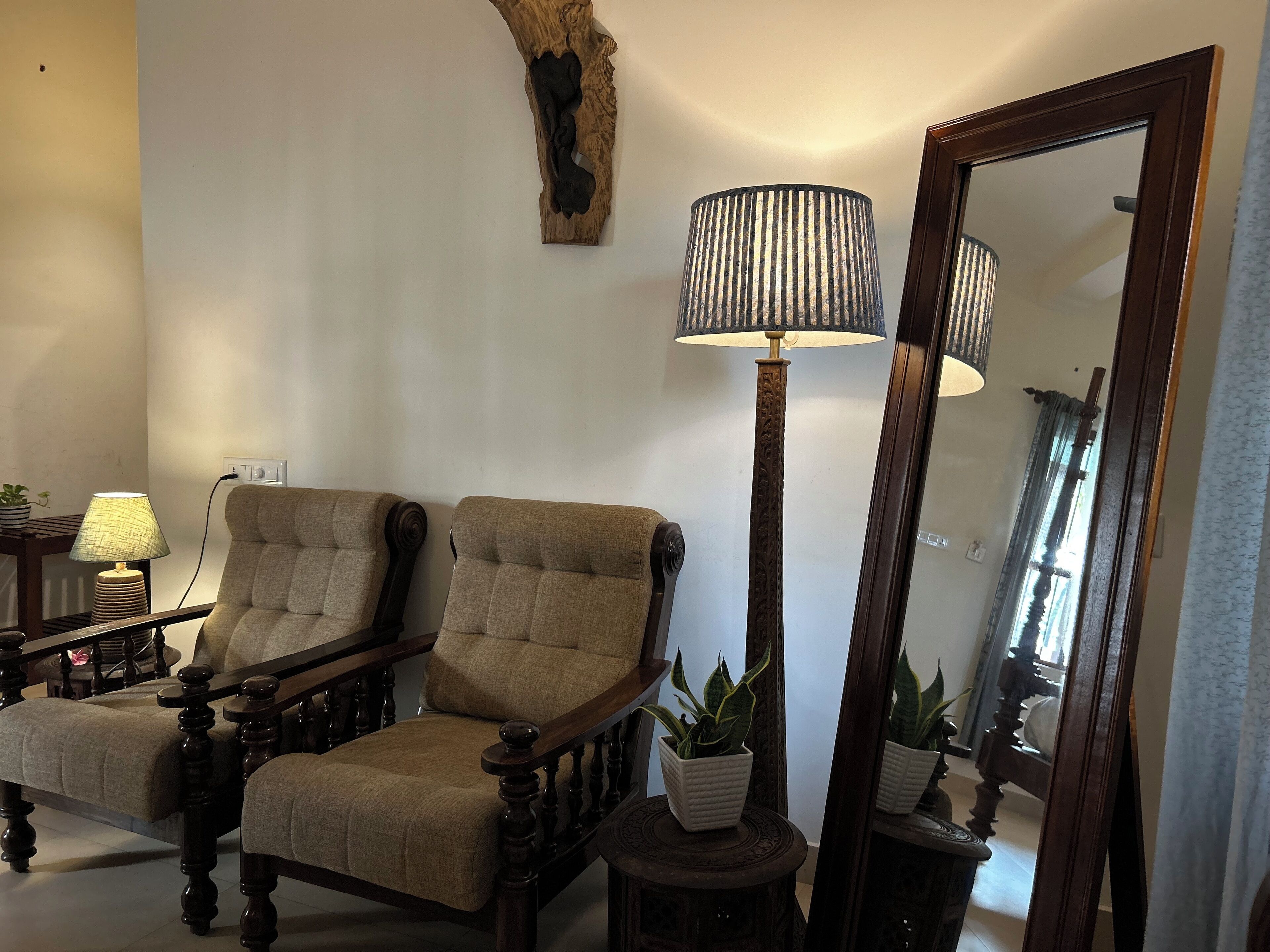 Un salón con dos sillones tapizados, una lámpara de pie alta, un espejo y una mesita con una planta en maceta.