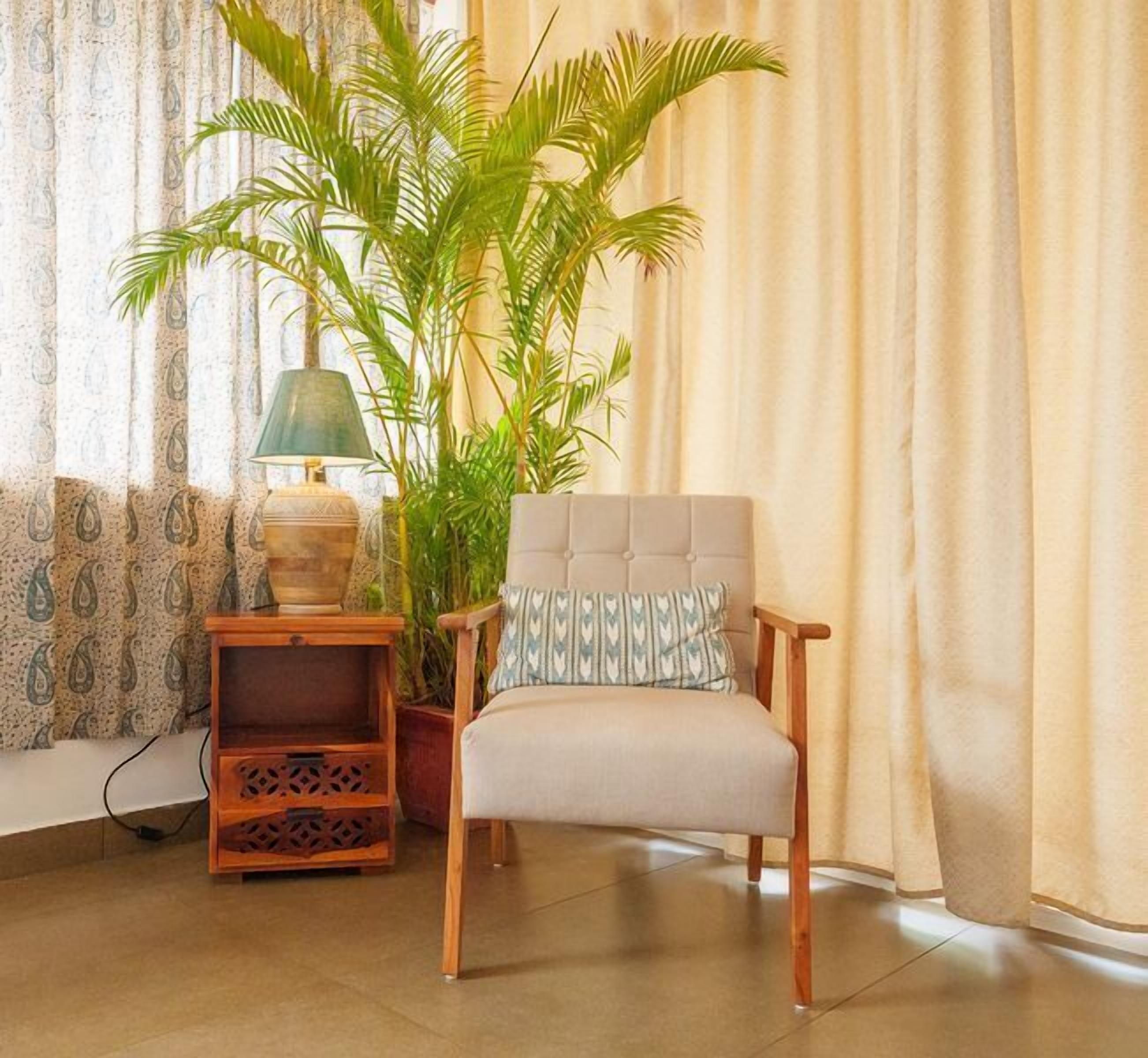 Una habitación con una silla, una lámpara, una planta y cortinas.