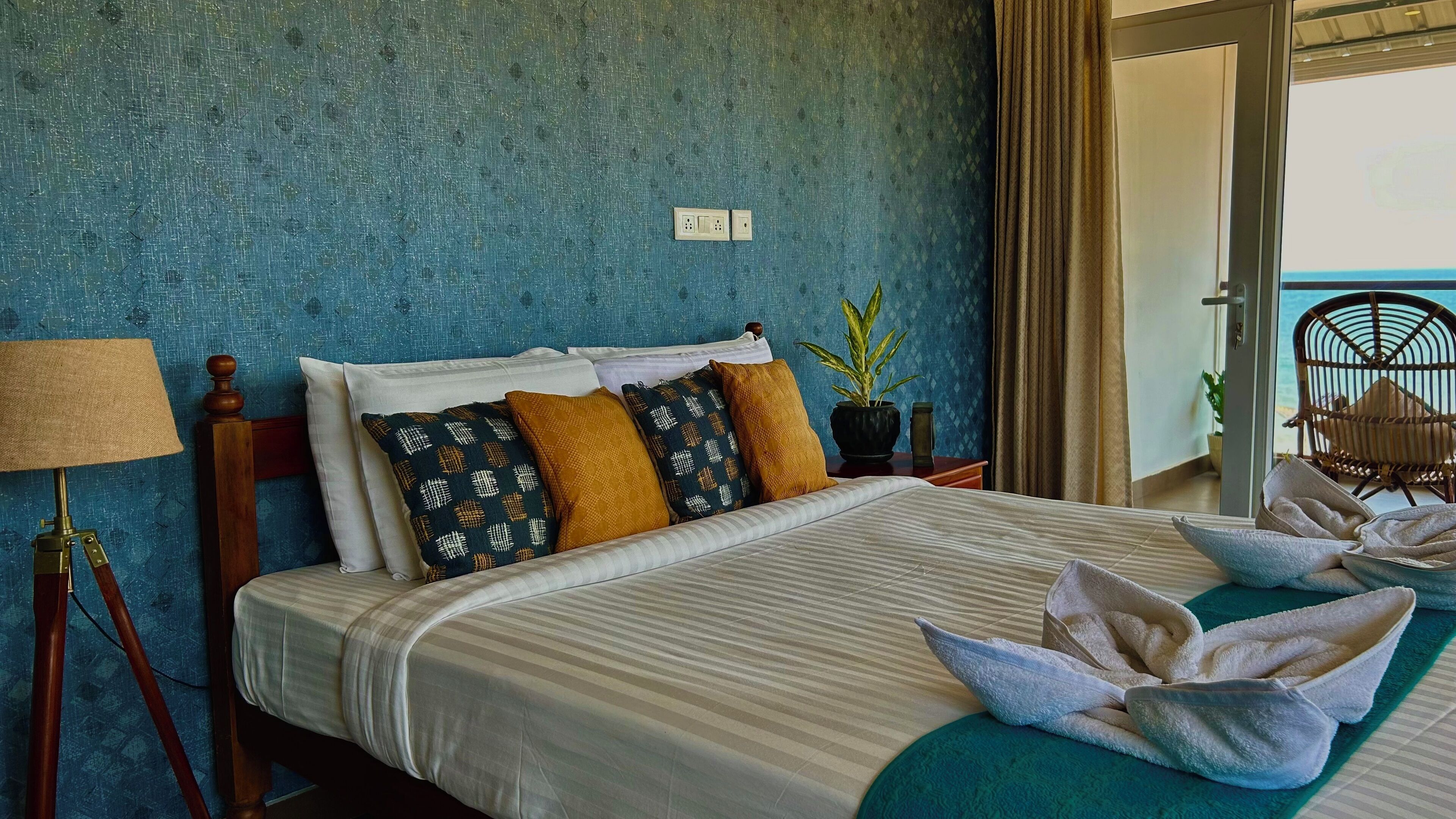 A neatly made bed with striped bedding, a lamp, and a potted plant on a nightstand.