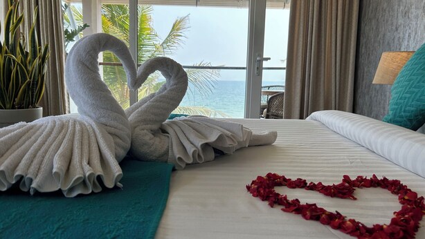 A hotel room with a bed, a heart-shaped arrangement of rose petals, and two towels shaped like swans.