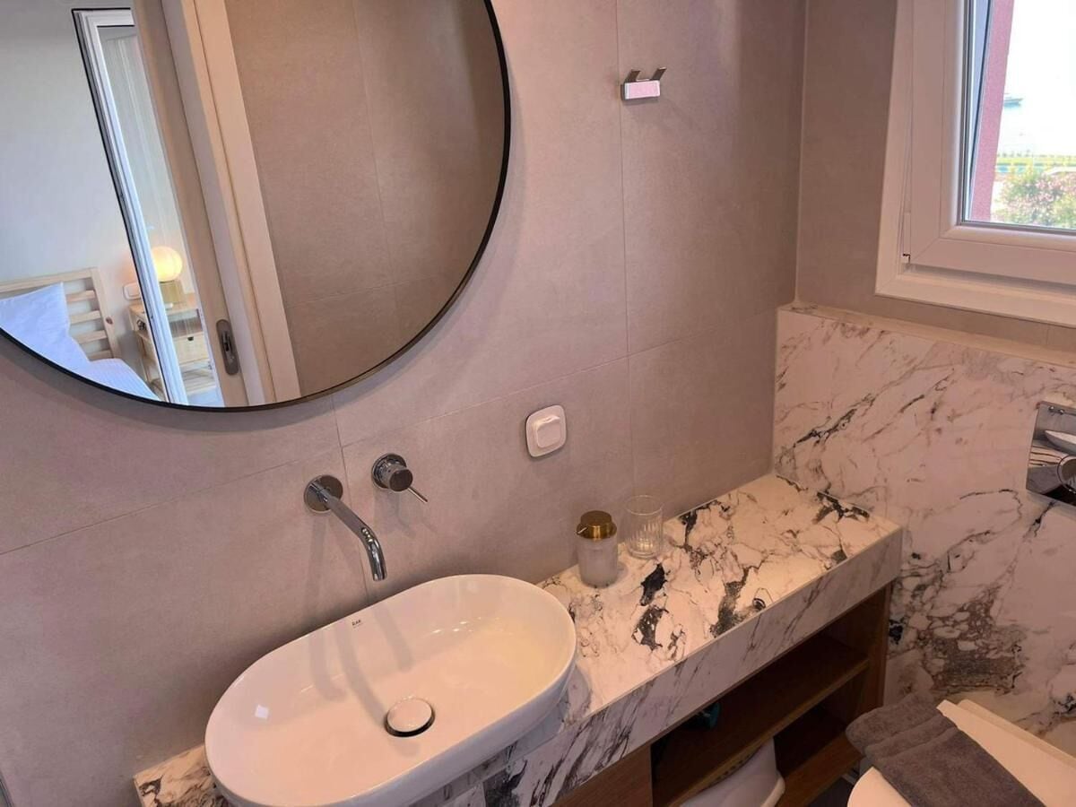 A bathroom with a round mirror, a white sink, and a marble countertop.