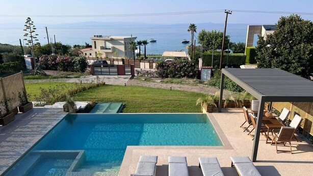 Una piscina con sillones de descanso y vista al mar.