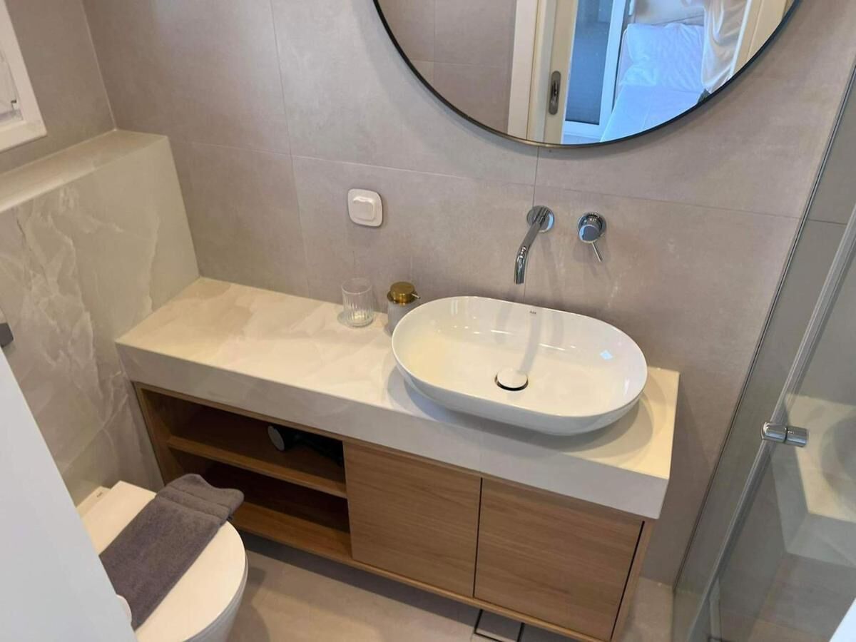 A bathroom with a round mirror, a white sink, and a toilet.